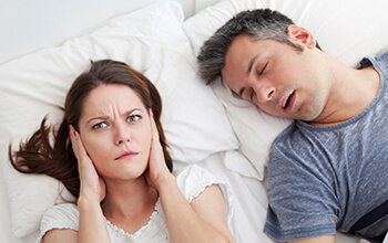 Snoring man and woman covering ears in bed