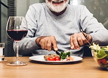 Man with dental implants in Westfield sitting at table, smiling, eating steak