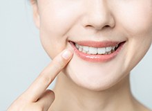 Closeup of smiling patient pointing to her dental implant in Westfield