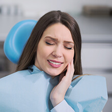 Woman in dental chair holding cheek in pain