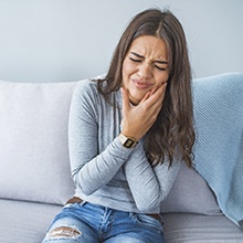 Woman on couch rubbing her jaw in pain