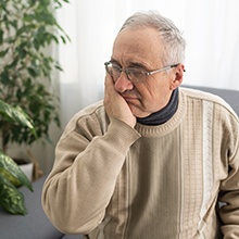 Man in sweater sitting on couch rubbing jaw