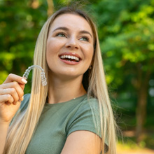 Woman in green shirt smiling and holding clear aligner