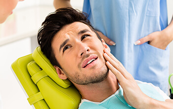 Man in dental chair holding cheek