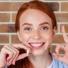 Smiling woman holding her tooth after tooth extractions in Westfield, NJ