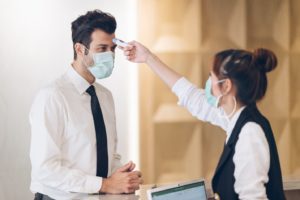 receptionist conducting contactless temperature check of incoming patient