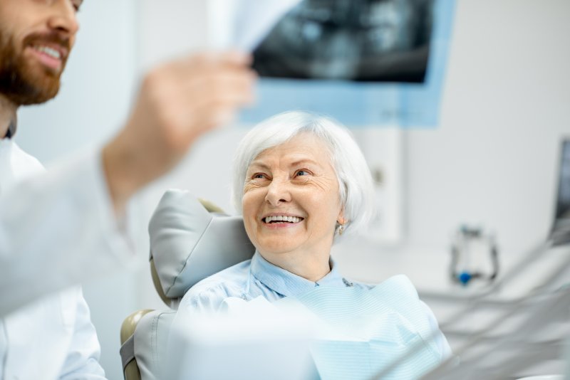 an older woman smiles while listening to her dentist during a checkup after receiving dental implants